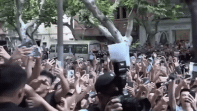 A Crowd Of People Are Holding Their Phones Up In The Air While A Man Takes A Picture Of Them . GIF