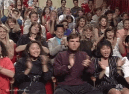 A Crowd Of People Are Sitting In A Room Applauding And Clapping . GIF