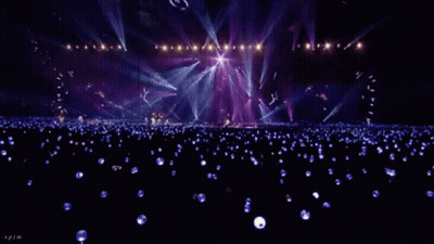 A Crowd Of People Are Sitting In A Stadium Watching A Concert With Purple Lights . GIF
