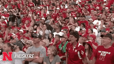 A Crowd Of People Are Sitting In A Stadium Wearing Red Shirts With The Letters N On Them . GIF