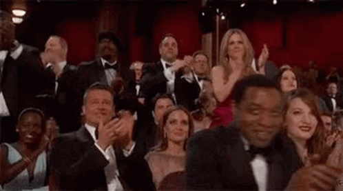 A Crowd Of People Are Sitting In A Theater Clapping . GIF