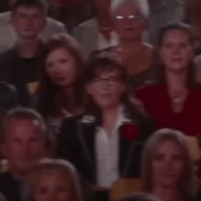 A Crowd Of People Are Sitting In A Theatre Watching A Show . GIF