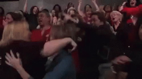 A Crowd Of People Are Standing In A Room With Their Arms In The Air And Screaming . GIF