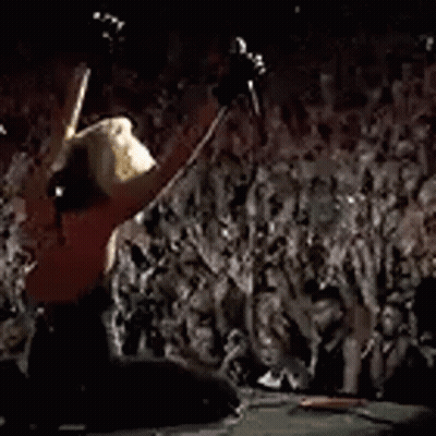A Crowd Of People Are Standing In Front Of A Stage Watching A Concert . GIF