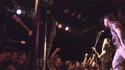 A Crowd Of People Are Watching A Band Perform On Stage With An Exit Sign In The Background GIF