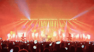 A Crowd Of People Are Watching A Concert With A Silhouette Of A Couple On Stage GIF