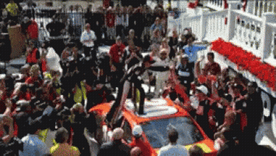 A Crowd Of People Gathered Around A Race Car GIF