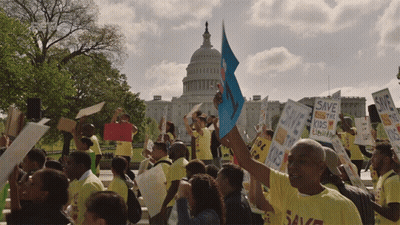 A Crowd Of People Holding Signs Including One That Says Save The Kids GIF