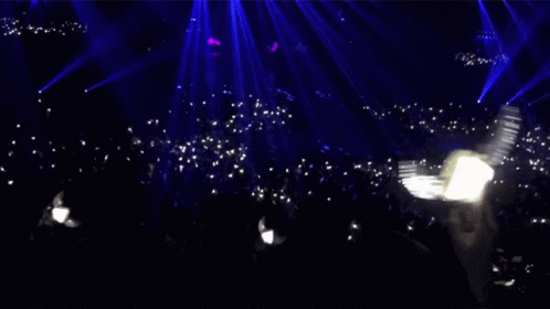 A Crowd Of People In A Dark Room With A Blue Light Behind Them GIF