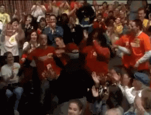 A Crowd Of People In Red Shirts Are Dancing And Clapping GIF