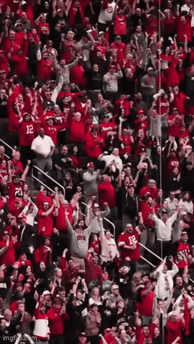 A Crowd Of People In Red Shirts Are Standing In A Stadium Watching A Game . GIF