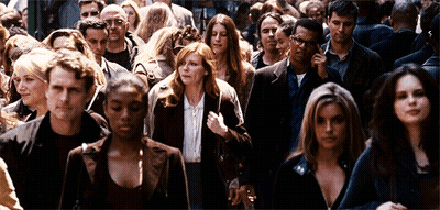 A Crowd Of People Walking Down A Street Including A Woman With Red Hair GIF
