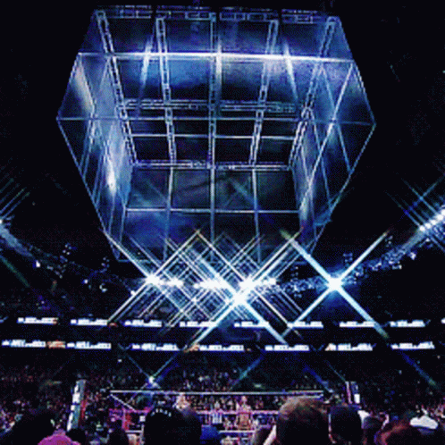 A Crowd Of People Watching A Wrestling Match In A Stadium With A Giant Cube In The Background GIF