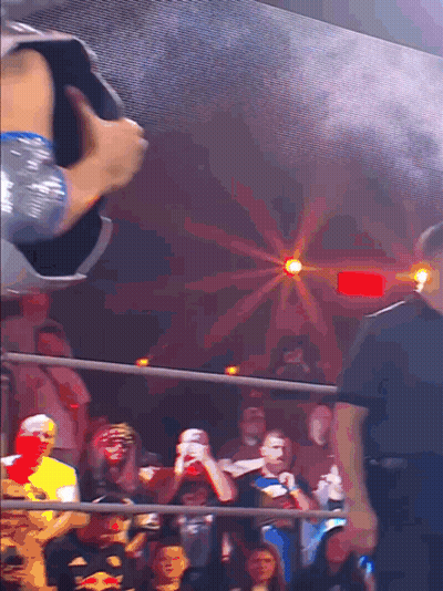 a crowd of people watching a wrestling match with a red light behind them