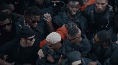 A Crowd Of People With One Wearing Sunglasses And A Necklace That Says Armour GIF