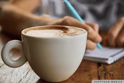 A Cup Of Coffee Sits On A Table Next To A Person Writing On A Notebook GIF