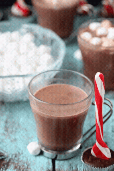 A Cup Of Hot Chocolate Next To A Candy Cane On A Table GIF