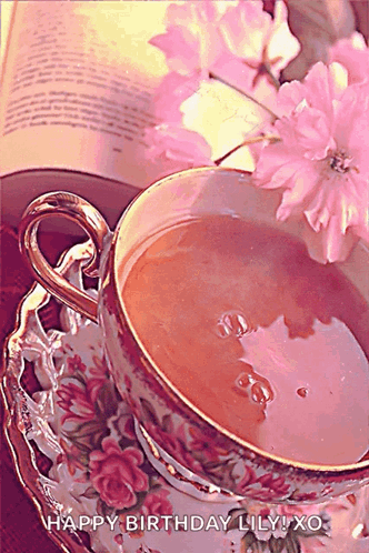 A Cup Of Tea Sits On A Saucer Next To A Book And Pink Flowers With The Words Happy Birthday Lily Xo GIF