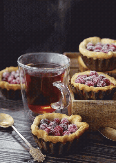A Cup Of Tea Sits On A Table Next To A Tray Of Muffins GIF