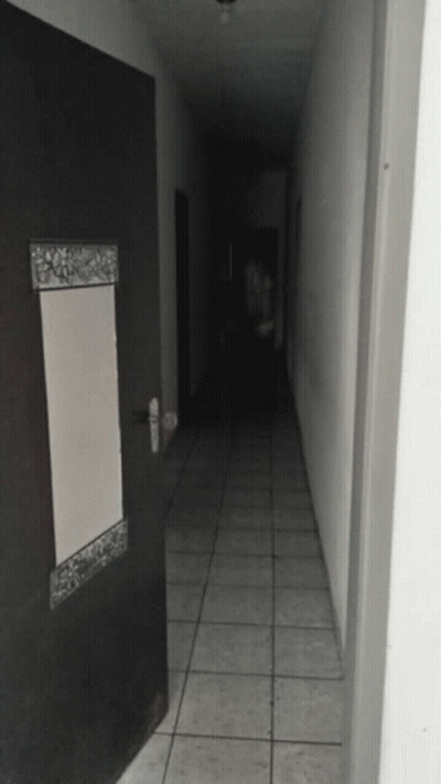 A Dark Hallway With A Door And A Mirror GIF