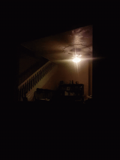 A Dark Room With A Staircase Leading Up To A Shelf With Pictures On It GIF
