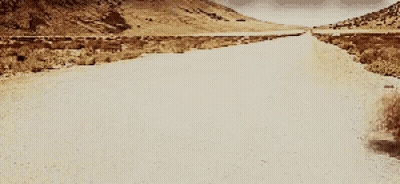 A Desert Road With Mountains In The Background GIF