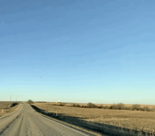 A Dirt Road Going Through A Field With A Blue Sky Behind It GIF