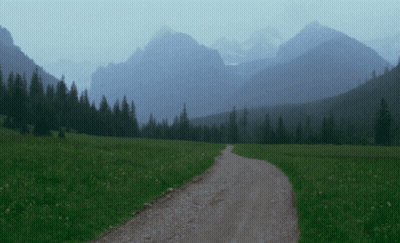 A Dirt Road Going Through A Grassy Field In The Mountains GIF