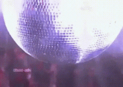 A Disco Ball Is Spinning In A Dark Room With Purple Lights . GIF