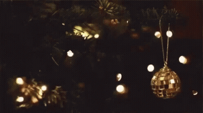 A Disco Ball Ornament Hangs From A Christmas Tree Branch GIF