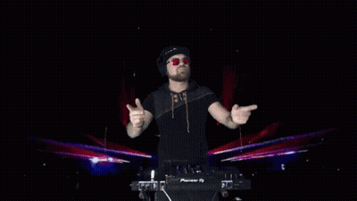 A Dj Wearing Headphones And Sunglasses Stands In Front Of A Pioneer Dj Controller GIF