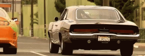 A Dodge Charger Is Driving Down A Street Next To Another Car With A License Plate That Says California GIF