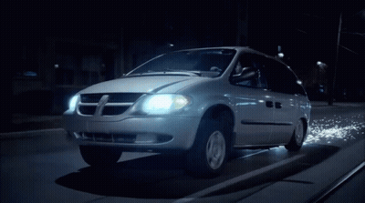 A Dodge Minivan Is Driving Down A Dark Street At Night GIF