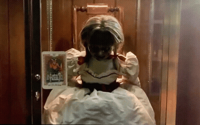 A Doll In A White Dress Is Sitting In A Chair Holding A Book GIF