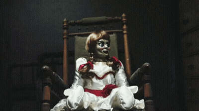 A Doll Is Sitting In A Chair With A Red Bow Around Her Neck GIF