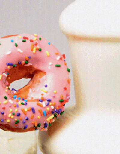 A Donut With Pink Frosting And Sprinkles Next To A Vase GIF