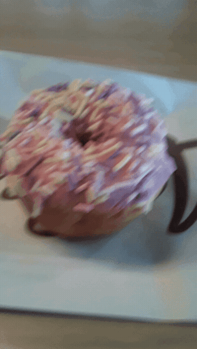 A Donut With Pink Frosting And Sprinkles On Top GIF