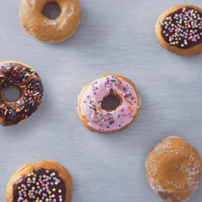 A Donut With Pink Frosting Is Surrounded By Other Donuts GIF