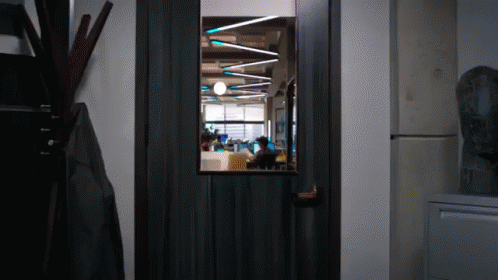A Door With A View Of A Room With People Working GIF