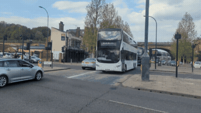 A Double Decker Bus Is Driving Down The Road GIF
