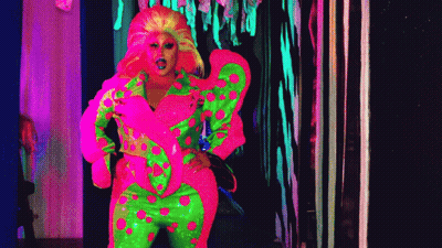 A Drag Queen In A Neon Pink And Green Outfit Is Standing In A Dark Hallway . GIF
