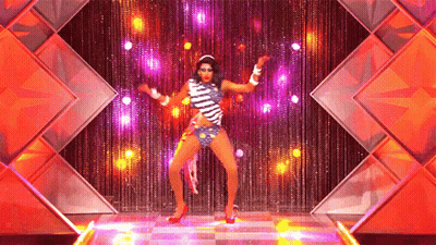 A Drag Queen Is Dancing On A Stage In Front Of A Curtain GIF