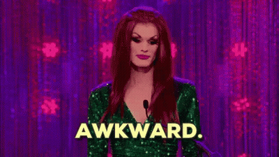 A Drag Queen Is Standing In Front Of A Microphone With The Word Awkward Written On It . GIF