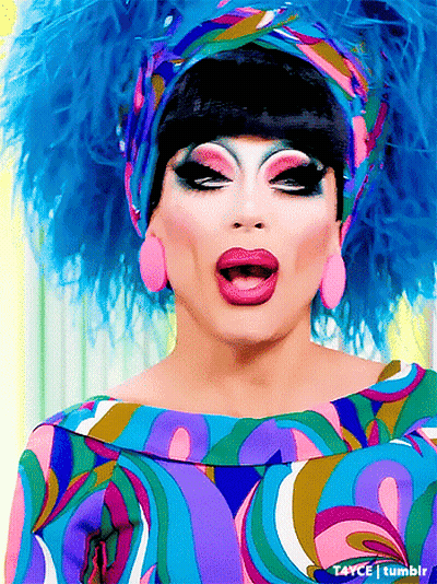 A Drag Queen Is Wearing A Colorful Dress And A Blue Headpiece GIF