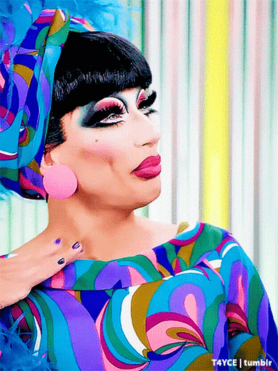 A Drag Queen Is Wearing A Colorful Dress And A Headband GIF