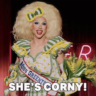 A Drag Queen Is Wearing A Miss Greenton Sash And Holding A Bouquet Of Yellow Flowers GIF