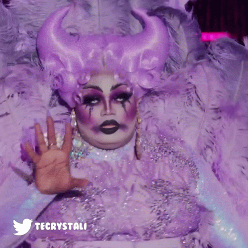 A Drag Queen Is Wearing A Purple Feathered Costume And A Twitter Logo GIF