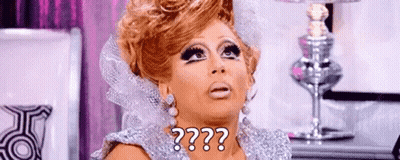 A Drag Queen Is Wearing A Silver Dress And Earrings And Making A Funny Face . GIF