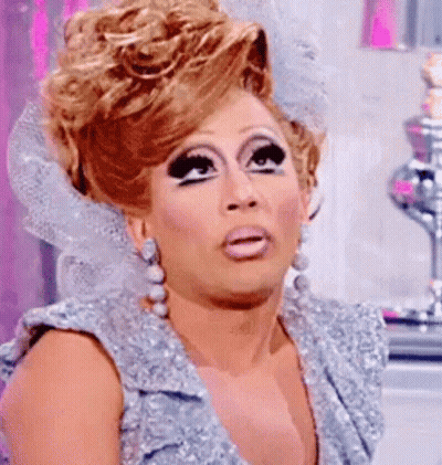 A Drag Queen Is Wearing A Silver Dress And Earrings And Making A Surprised Face . GIF