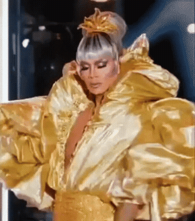 A Drag Queen Is Wearing A Very Large Gold Dress And A Crown On Her Head . GIF